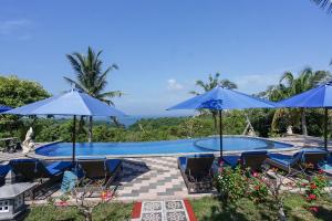 a swimming pool with blue umbrellas and chairs at Penida Sunset Ocean View Bungalows in Nusa Penida