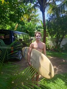 un hombre sosteniendo una tabla de surf delante de un coche en Ocean edge villa, en Midigama East