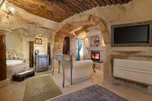a stone bathroom with a tub and a tv at Elysion Cave Suites in Urgup