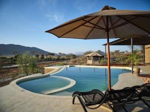a swimming pool with two chairs and an umbrella at Surana Buffalo Springs in Buffalo Springs  National Reserve