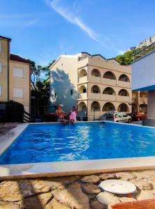 2 persone sedute accanto a una grande piscina blu di Apartments Vila Adrijana & Fitness Studio WOLF BV a Baška Voda