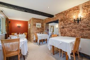 a restaurant with white tables and chairs and a brick wall at Castle Of Comfort Hotel in Nether Stowey