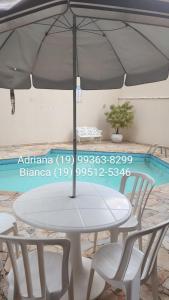 een tafel en stoelen met een parasol naast een zwembad bij Enseada Guarujá Ap214 in Guarujá