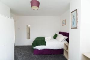 a bedroom with a bed with white walls and a purple couch at Foxwood Stays in Leeds
