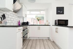 a white kitchen with white cabinets and a window at Foxwood Stays in Leeds