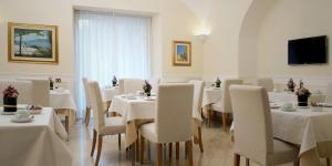 un restaurante con mesas y sillas blancas y TV en Hotel Plaza, en Salerno