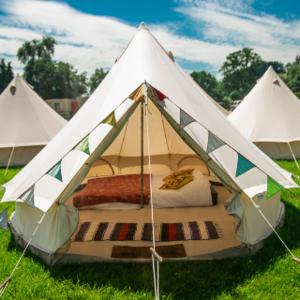 a bed in a white tent in the grass at Fred's Yurts at Hay Festival in Hay-on-Wye