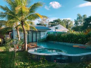 a swimming pool in front of a house with a palm tree at Khu Nghỉ Dưỡng Green Bungalow Phu Quoc in Phu Quoc