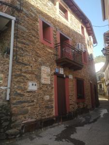 a brick building with red doors and a balcony at Casa Rural El Chorritero in Ovejuela