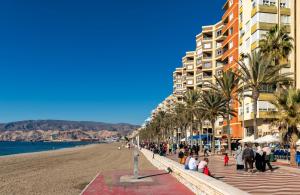um grupo de pessoas caminhando ao longo de uma praia com edifícios em Apartamento Zapillo a 3 minutos de la playa em Almeria