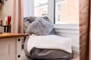a grey chair with a pillow and a window at The Cosy Norse Retreat in York