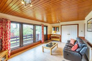 uma sala de estar com um sofá de couro e janelas grandes em Bluebell Lodge 2 with Hot Tub em Newton Stewart