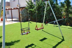 two swings in a yard with green grass at Lagos Studios & Apartments in Palekastron