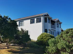 a white house on top of a hill with trees at Struispaleis in Struisbaai