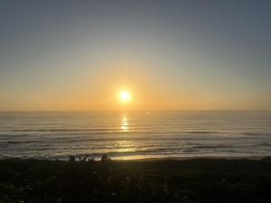 a sunset over the ocean with people standing on the beach at Beach Escape on the coast at apartment 78 Sancta Maria in Amanzimtoti
