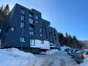 a black building with cars parked in the snow at Apartman LENA in Bjelašnica