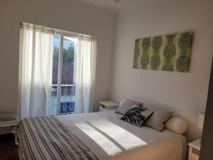 a white bedroom with a bed and a window at Beach and Surf House in Costa da Caparica
