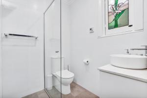 a white bathroom with a toilet and a sink at Noir Cottage Glenelg North in Glenelg