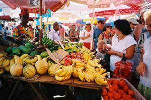 Un groupe de personnes autour d'un stand de fruits sur un marché dans l'établissement Catamaran TAO, à Sainte-Anne