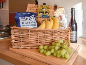 a basket of fruit and grapes on a counter with a bottle of wine at Blacksmiths Cottage in Upwey