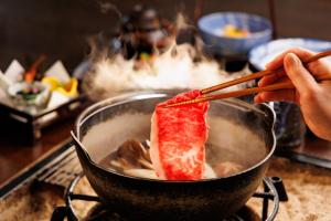 een persoon roert voedsel in een wok met eetstokjes bij Hotel Yamabuki in Komagane