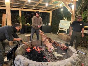 un grupo de hombres parados alrededor de una parrilla con carne en Hotel & Cava Estancia Rilán, en Castro