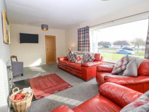 a living room with red leather furniture and a large window at Cae Glas in Pwllheli