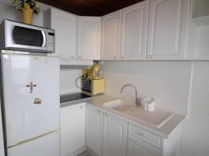 a kitchen with white cabinets and a sink and a microwave at Studio Cabine Rénové au Pied des Pistes avec Balcon - Auris en Oisans - FR-1-297-157 in Auris
