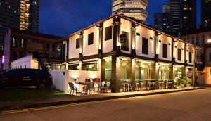 a building with tables and chairs on a street at night at Dream Chaser Boutique Capsule Hotel in Singapore