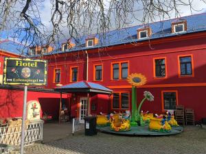 a red building with a hotel with a playground in front at Hotel Eulenspiegel - Das Erlebnishotel in Riesa in Riesa