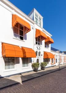 ein weißes Gebäude mit orangefarbenen Sonnenschirmen auf einer Straße in der Unterkunft Strandhotel Wilhelmina in Domburg