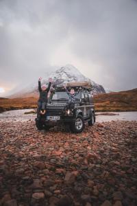 dos personas sentadas en la parte trasera de un jeep delante de una montaña en Land Rover Defender Luxury Camper, en Morpeth