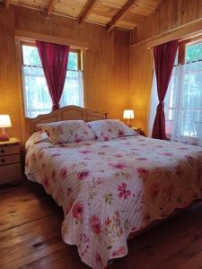 a bedroom with a bed with a floral bedspread and two windows at Cabaña del Volcán in Licán Ray