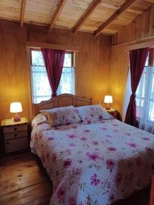 1 dormitorio con 1 cama con colcha de flores y 2 ventanas en Cabaña del Volcán, en Licán Ray