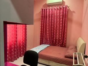 a bedroom with red curtains and a bed with a chair at Homestay Rohmat in Kota Bharu