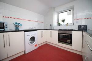 a white kitchen with a washing machine and a window at Stunning 4 Bedroom Flat near City Centre in Swansea