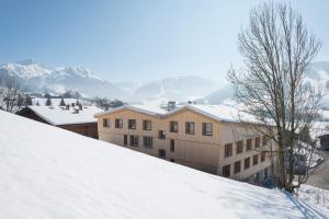 a building on a snow covered hill with mountains in the background at Gstaad Saanenland Youth Hostel in Gstaad