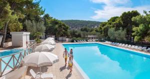 a group of people standing next to a swimming pool with umbrellas at Gattarella Family Resort - Self catering accommodations in the pinewood in Vieste