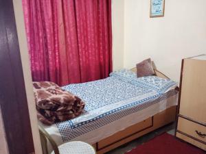 ein kleines Bett in einem Zimmer mit einem roten Vorhang in der Unterkunft Benus in Darjeeling