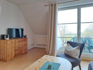 uma sala de estar com uma televisão, uma cadeira e uma mesa em Ruhepol am Meer - Apartment mit Balkon em Bastorf