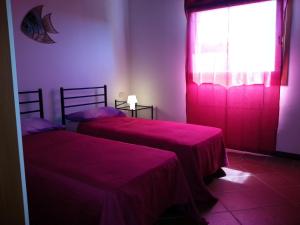 a bedroom with two beds and a window with pink sheets at Villa Serena B in Stintino