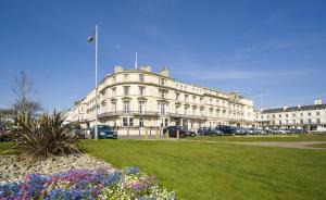 ein großes weißes Gebäude mit Autos auf einem Parkplatz in der Unterkunft The Carlton Hotel in Great Yarmouth