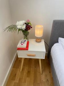 una mesita de noche con un jarrón de flores y un libro en Cosy studio flat for students or workers. en Bedford