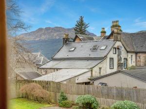 Una casa antigua con una valla y montañas al fondo. en Cheerful Stays: 4 Bedroom Cottage in Arrochar, en Arrochar