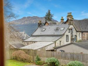 an old house with a fence and mountains in the background at Cheerful Stays: 4 Bedroom Cottage in Arrochar in Arrochar