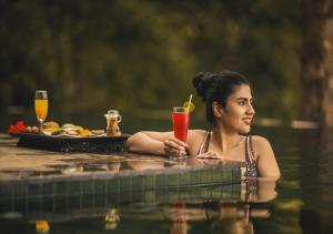 Eine Frau, die mit einem Drink im Wasser sitzt. in der Unterkunft Chembarathi Wayanad Boutique Resort in Vaduvanchal