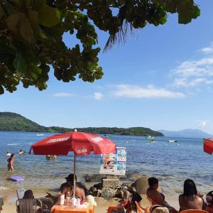 a group of people sitting on a beach under an umbrella at Pousadinha Ateliê da Maite in Paraty