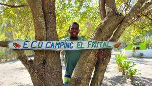Ein Mann, der in einem Baum steht und ein Surfbrett hält. in der Unterkunft Eco-Camping El Frutal in Isla Grande