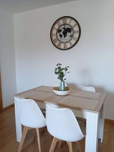 a dining room table with white chairs and a clock at Apartamento Area Maior in Malpica