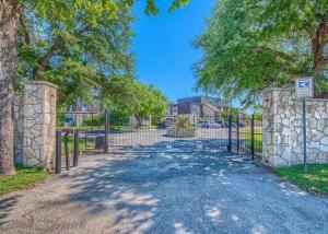 a gate to a driveway with trees and a building at Guadalupe Getaway in New Braunfels